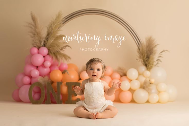 a baby sitting on the floor in front of some balloons and other decorations for a cake smash