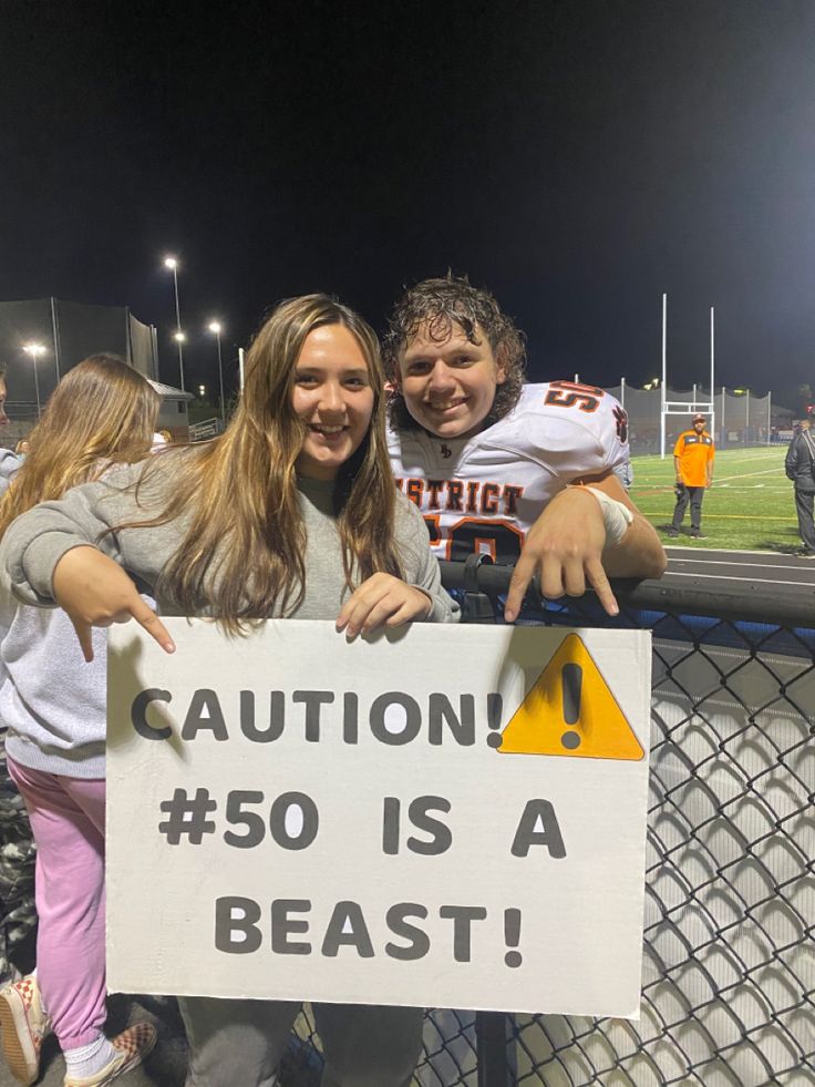 two people posing with a sign that says caution 50 is a beast