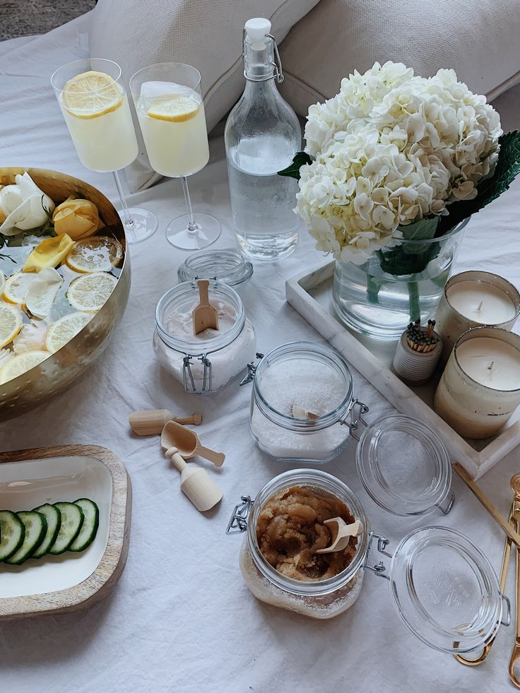 an assortment of food and drinks on a white tablecloth with flowers in vases