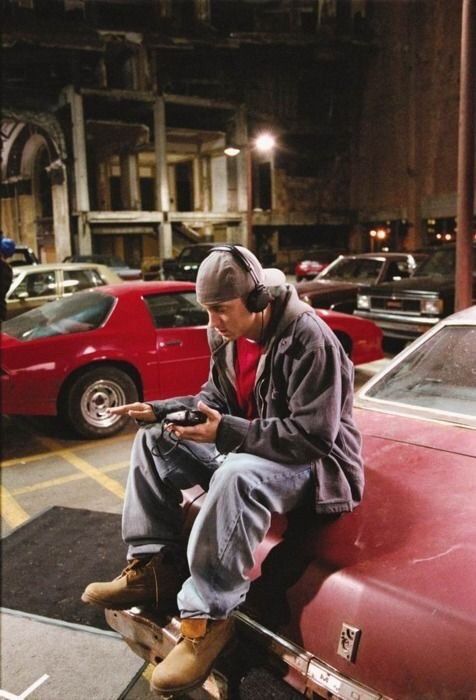 a man sitting on top of a red car while looking at his cell phone