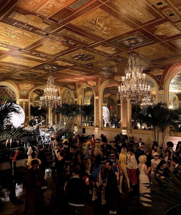 a large group of people standing in a room with chandeliers hanging from the ceiling