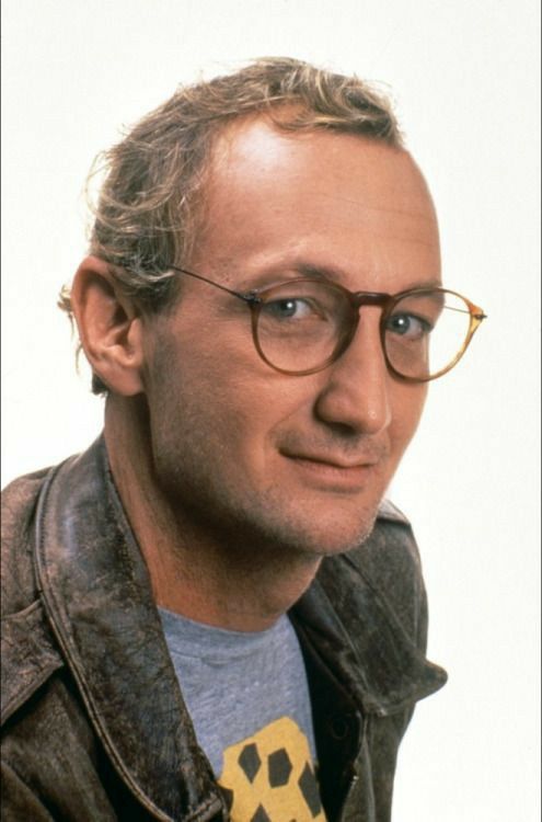 a man with glasses and a yellow tie is looking at the camera while wearing a leather jacket