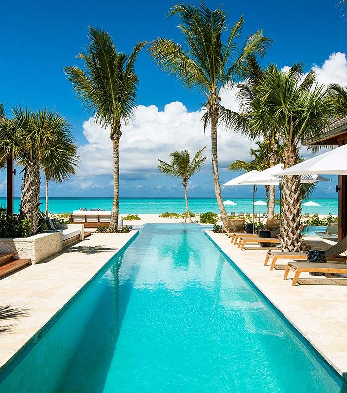 an empty swimming pool surrounded by palm trees near the beach with chairs and umbrellas