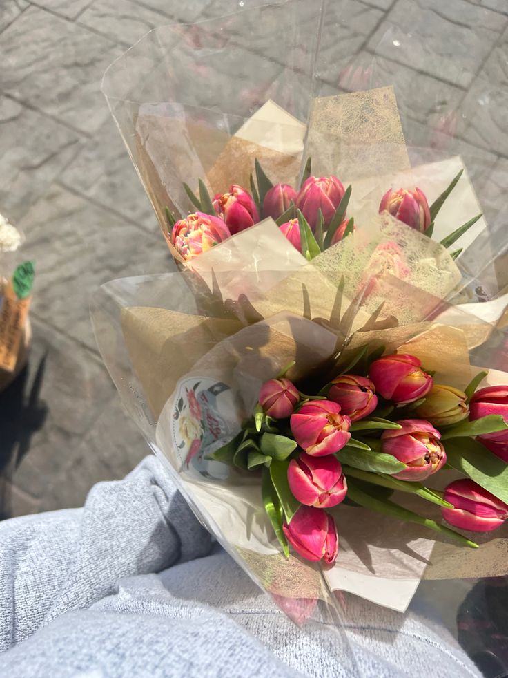 a bouquet of tulips is wrapped in clear cellophane and placed on someone's lap