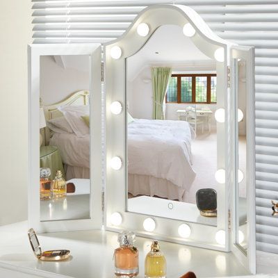 a white vanity mirror sitting on top of a table next to a dresser with lights