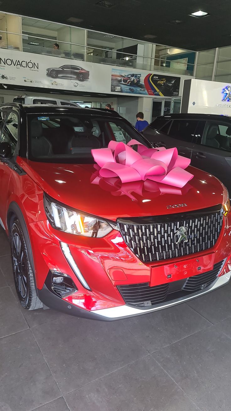 a red car with a pink bow on it's hood in a showroom