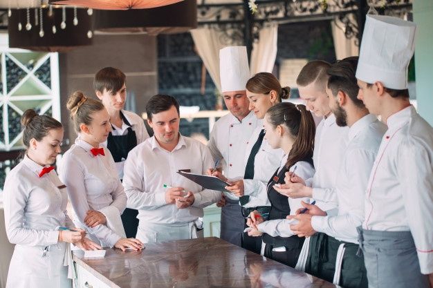 a group of people standing around a wooden counter in a kitchen with chefs on it