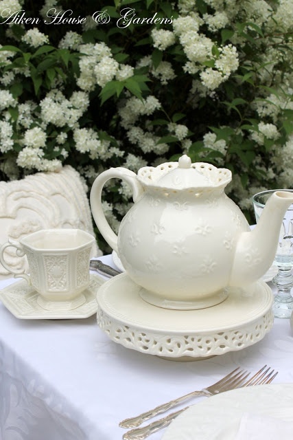 a white tea pot sitting on top of a table next to cups and saucers