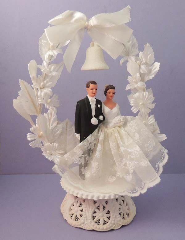 a wedding cake topper with a bride and groom under a bell on the table