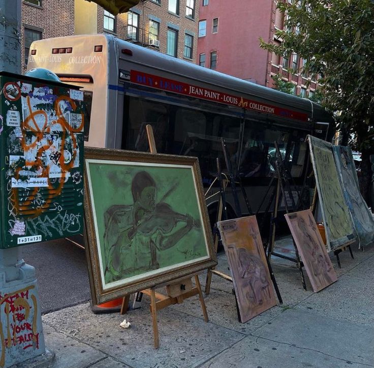 paintings are on the sidewalk next to a bus