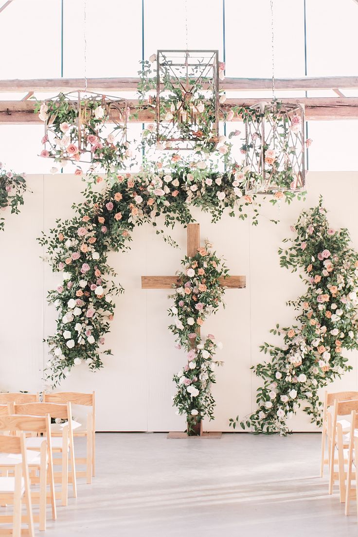 a cross decorated with flowers and greenery in front of a white wall at a wedding