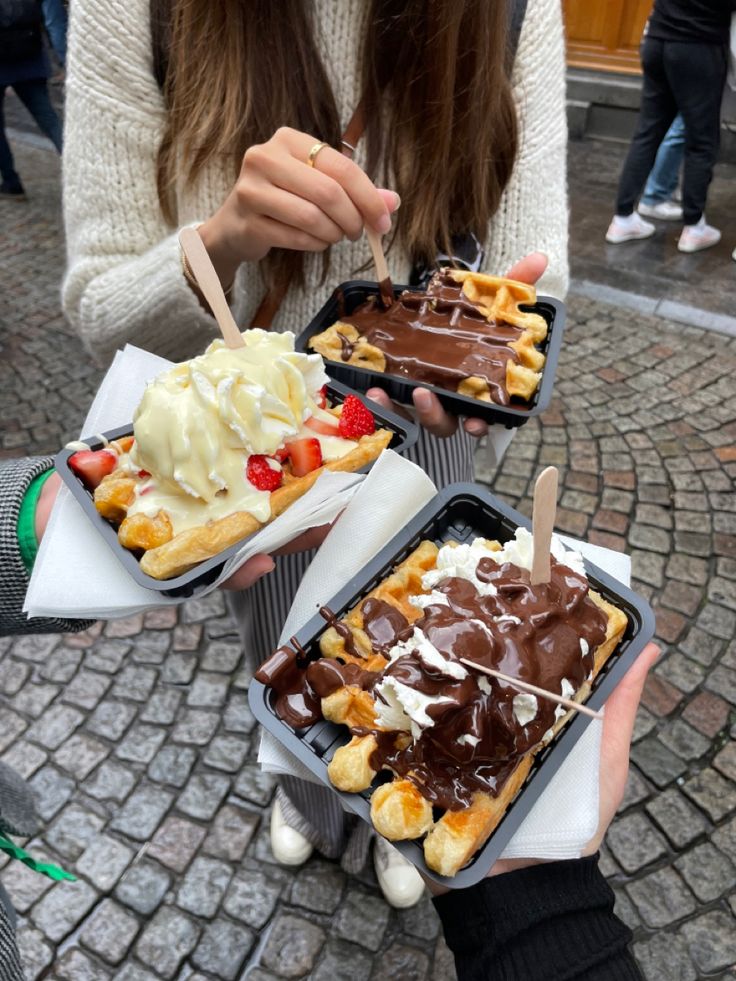 two people holding trays of food with ice cream and waffles on them