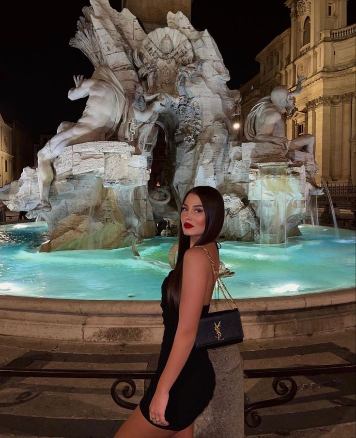 a woman standing in front of a fountain at night