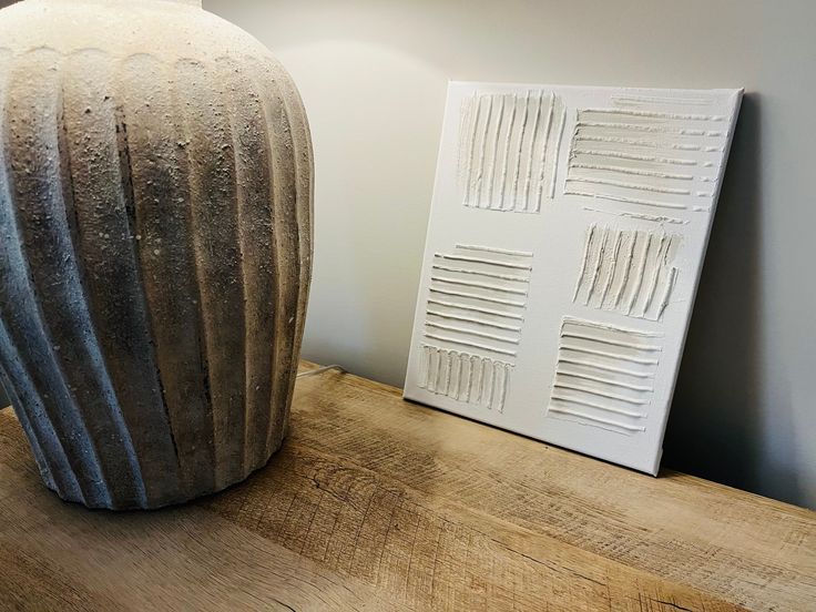 a white vase sitting on top of a wooden table next to a framed piece of art