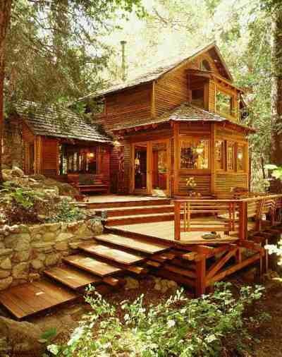 a wooden cabin in the woods with stairs leading up to it's porch and deck