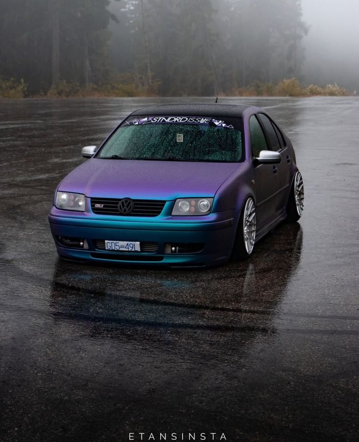 a purple and blue car parked in a parking lot on a rainy day with fog