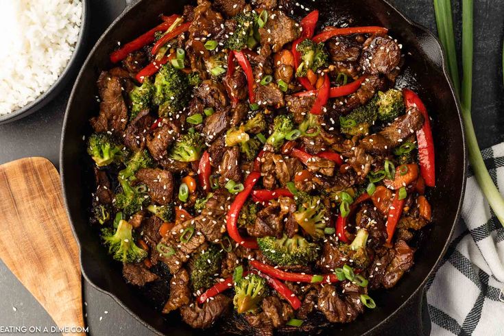 beef and broccoli stir fry in a skillet with rice on the side