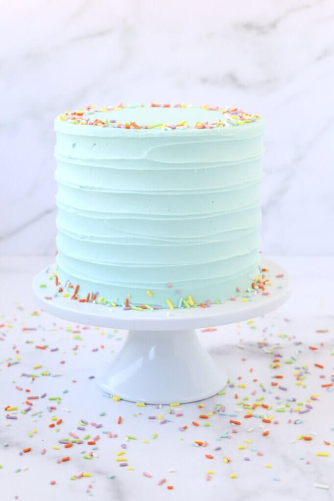 a frosted cake with sprinkles on a white pedestal and marble background