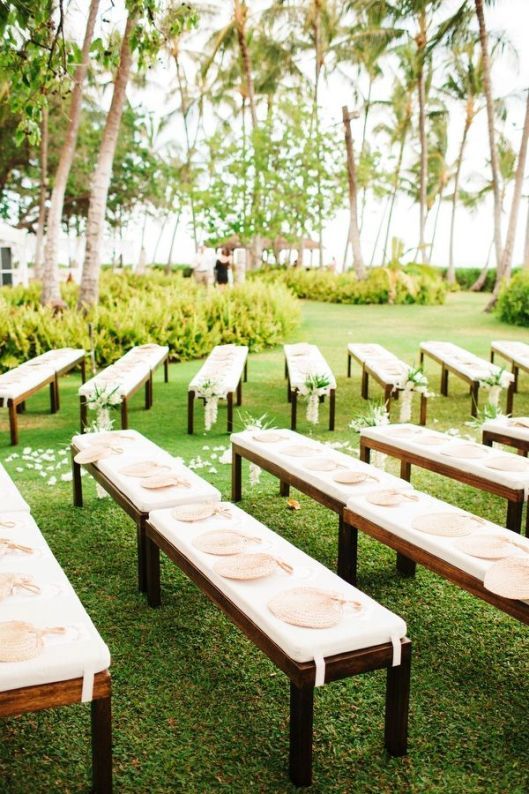 a row of benches sitting on top of a lush green field next to palm trees