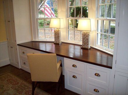 a desk with two lamps on it in front of some windows and a chair next to it