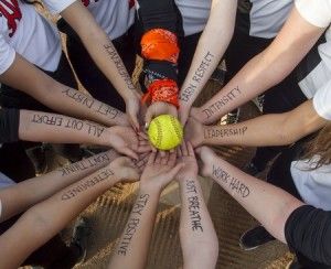 a group of people with their hands on top of a ball and the words softball written all over them