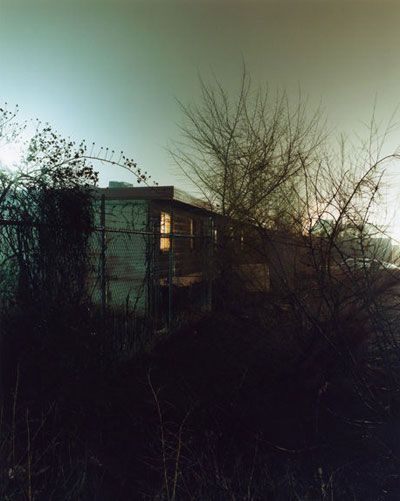 the sun is shining behind some trees and bushes in front of an abandoned building on a hill