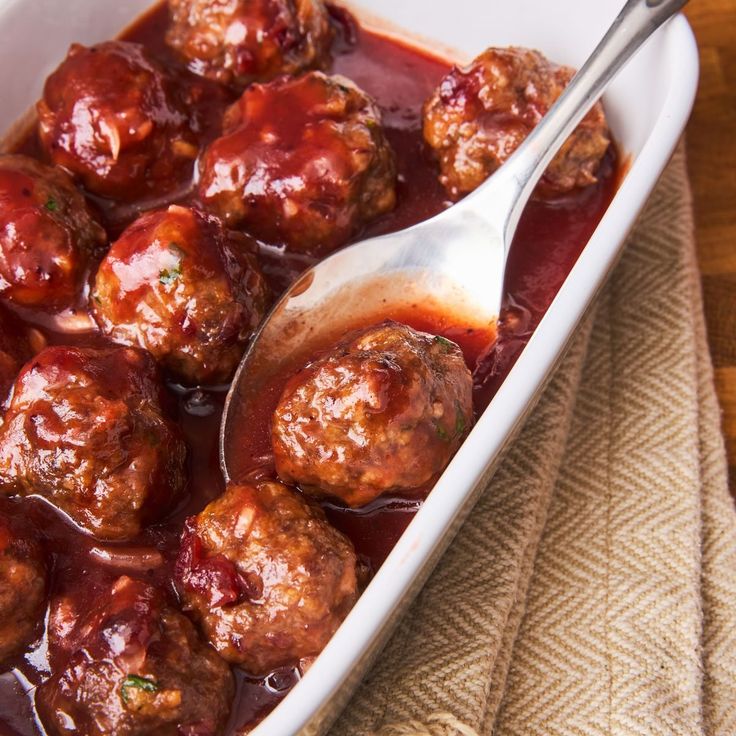 meatballs and sauce in a white casserole dish with a spoon on the side