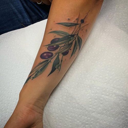 a woman's arm with olives and leaves on it