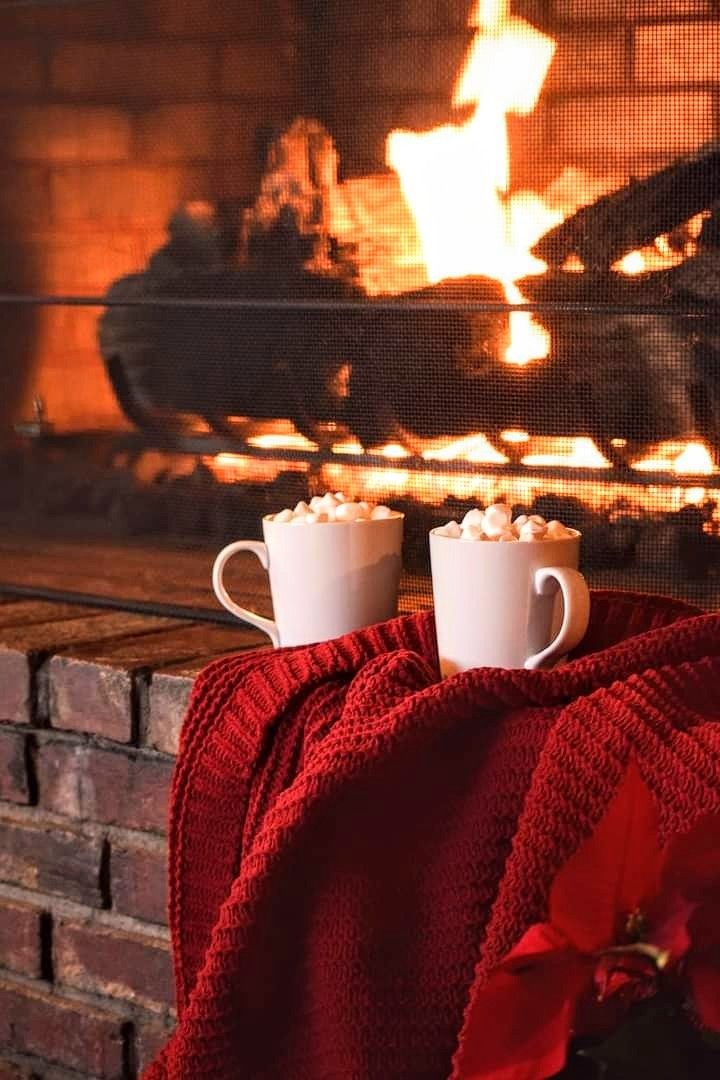 two cups of hot chocolate sitting in front of a fireplace