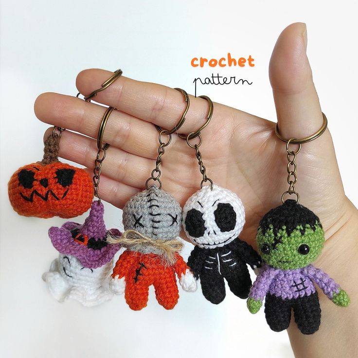 the hand is holding four small crocheted keychains with halloween decorations on them