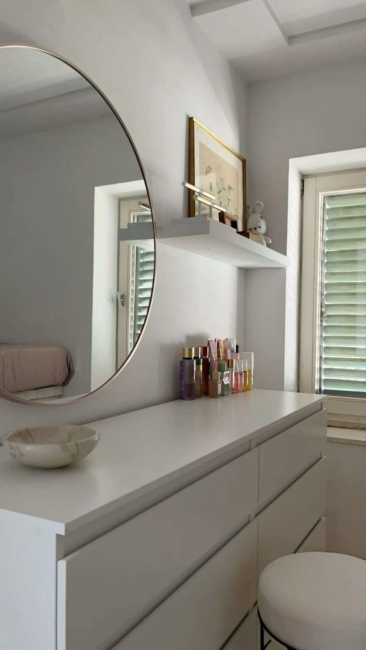 a white bathroom with a round mirror above the vanity and stool in front of it