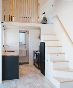 a kitchen and stairs in a small room with white walls, wood flooring and black appliances