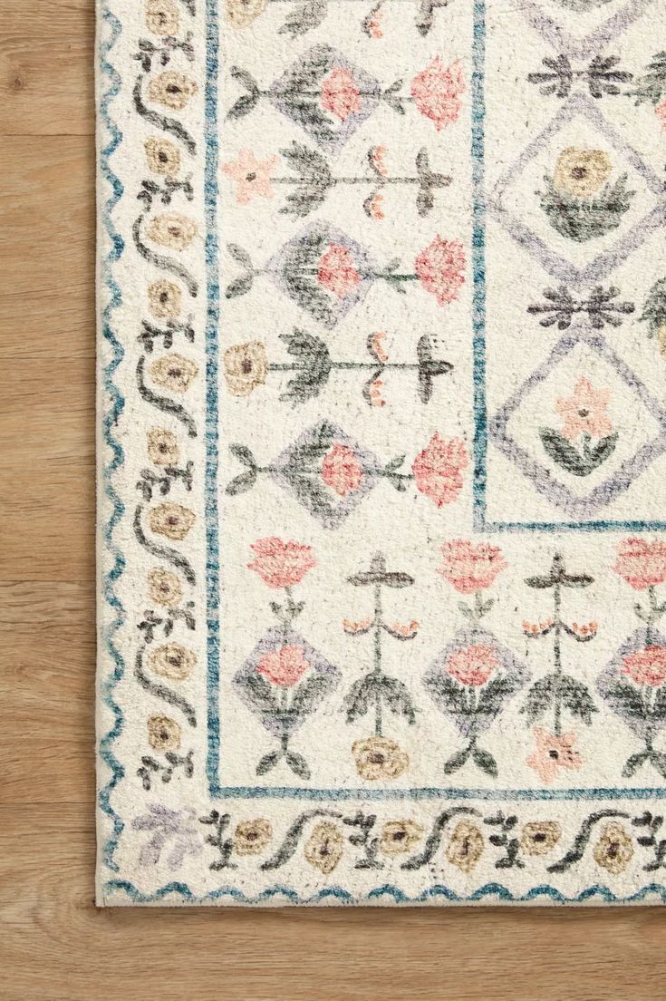 a white rug with pink flowers and blue trimmings on top of a wooden floor