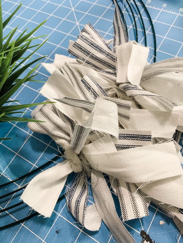 some scissors are laying on a table with strips of fabric next to it and a potted plant