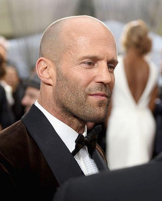 a bald man in a tuxedo and bow tie looks off to the side