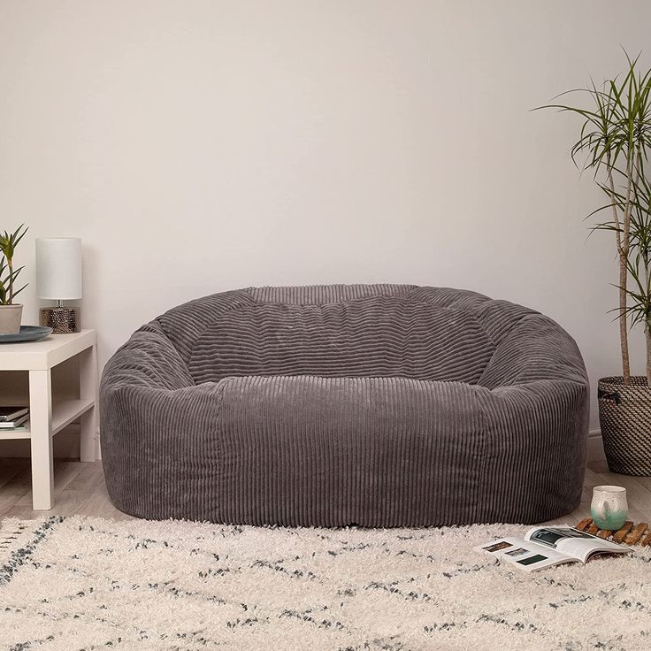 a large gray corded dog bed on a rug in a living room with potted plants