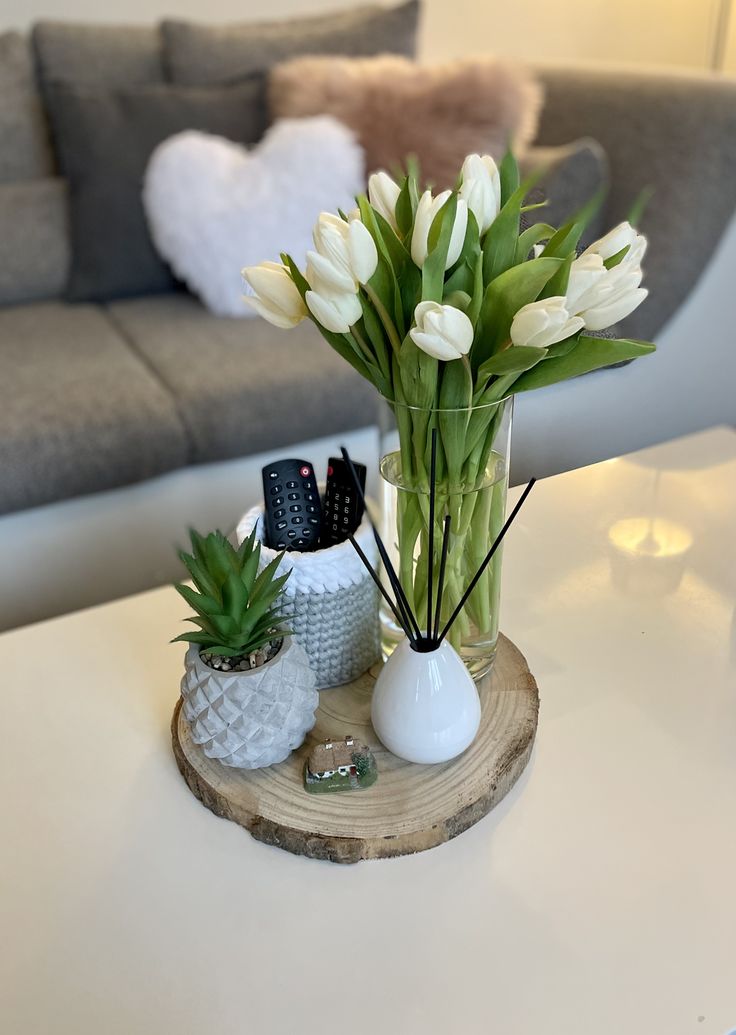 a vase with white flowers and pineapples on a wooden tray in front of a couch