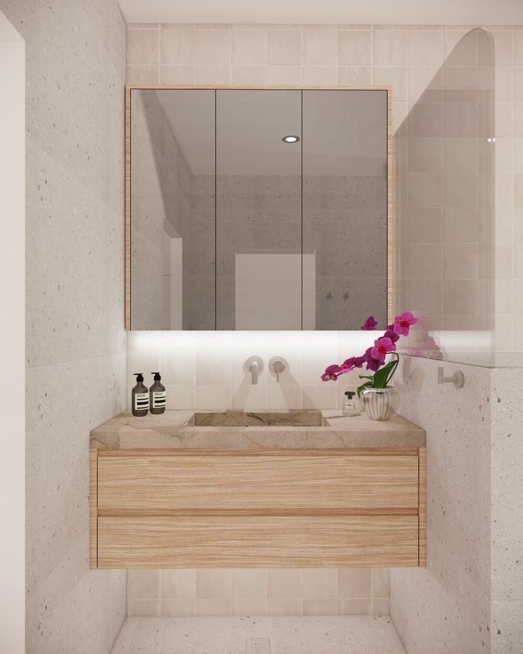 a bathroom with a sink, mirror and flowers in vase on the counter top next to it