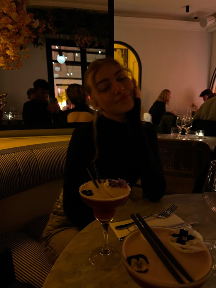 a woman sitting at a table with a drink in front of her