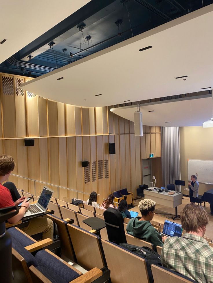 several people sitting in chairs with laptops on their laps and one person standing at the front of the room