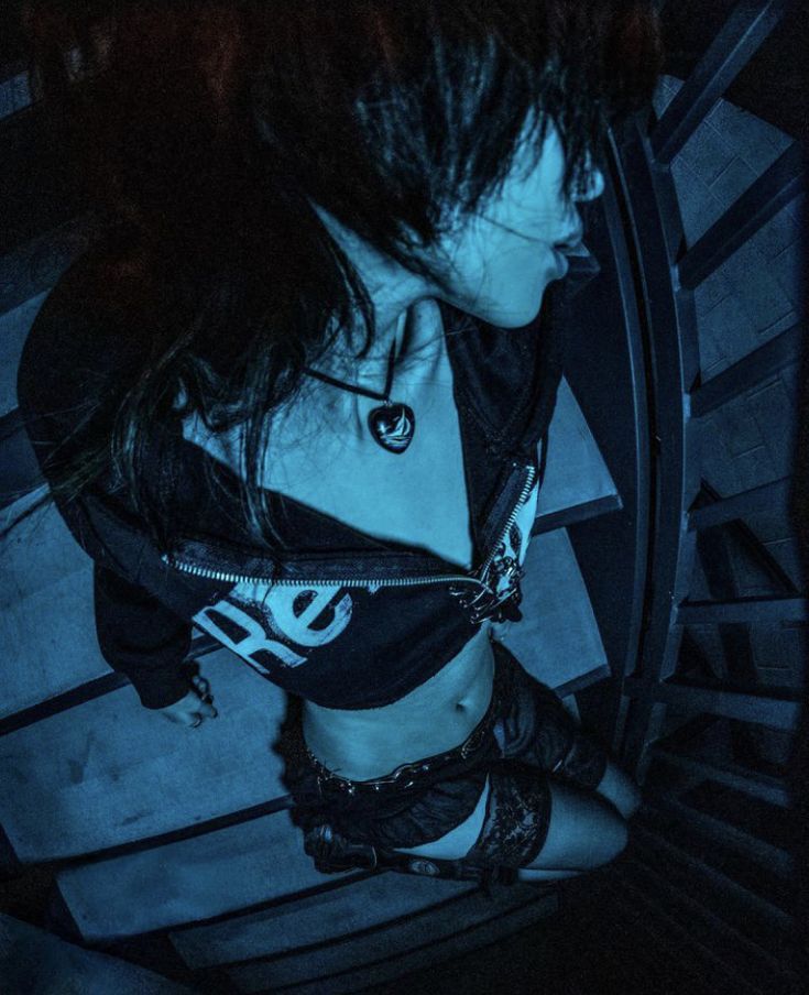 a woman with black hair and piercings standing in front of a clock