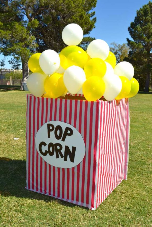 a popcorn bag filled with yellow and white balloons sitting on top of a grass covered field