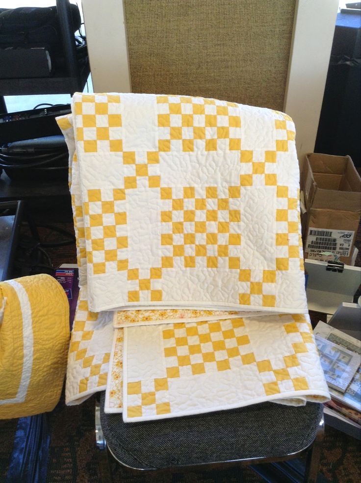 two yellow and white quilts sitting on top of each other in front of a chair