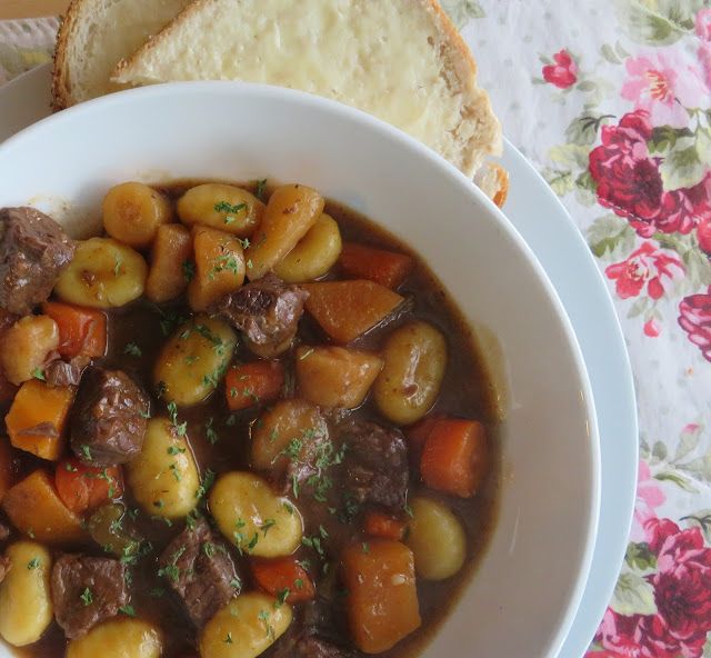 a white bowl filled with stew next to a slice of bread on top of a table