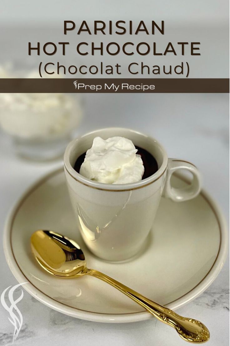 a cup of hot chocolate with whipped cream in it on a saucer and gold spoon