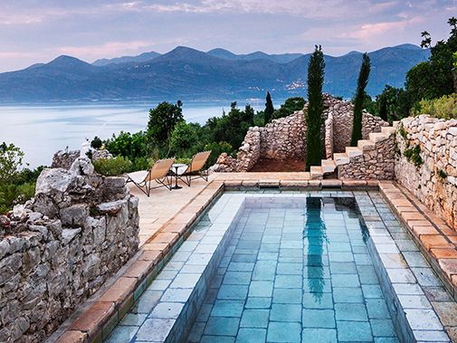 an outdoor swimming pool surrounded by stone walls and trees with mountains in the back ground