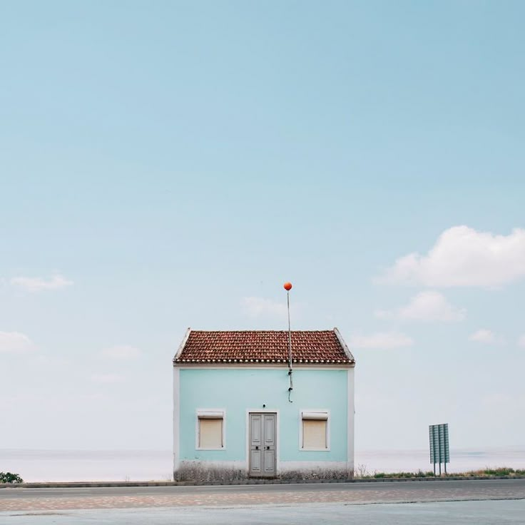 a small blue building with a red flag on it's roof next to the ocean