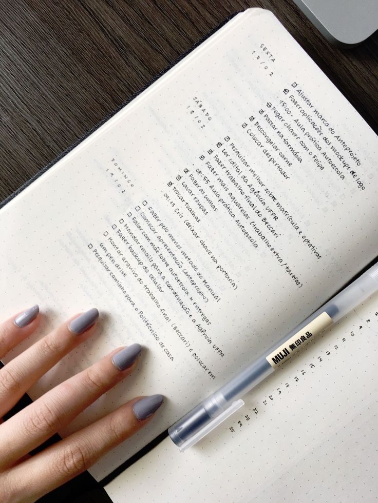 a woman's hand holding a pen next to an open book