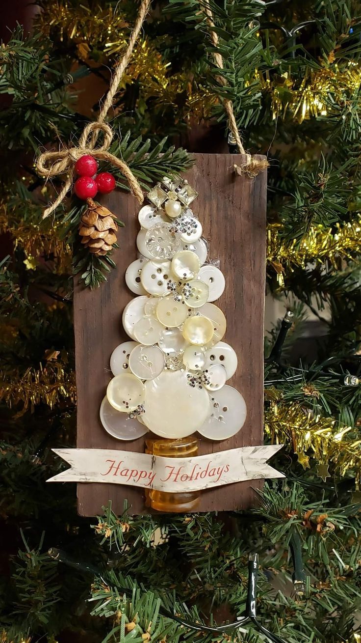 a christmas tree ornament hanging from a wooden plaque with buttons and pine cones on it