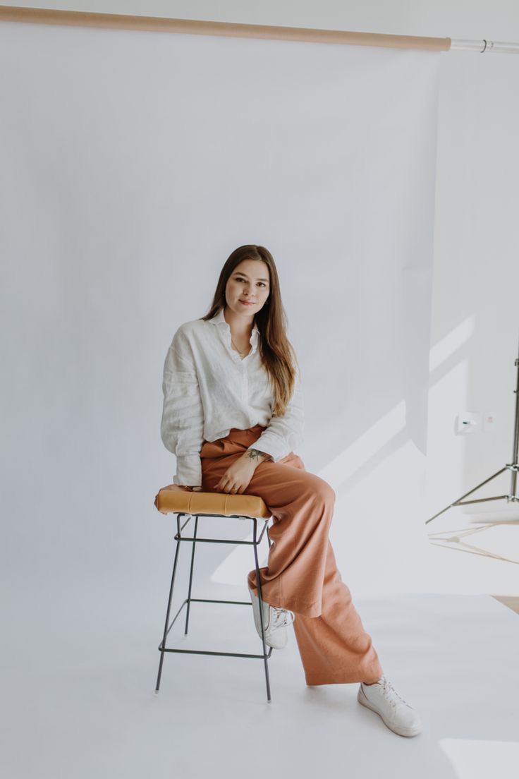 a woman sitting on top of a chair in front of a white wall and lighting equipment